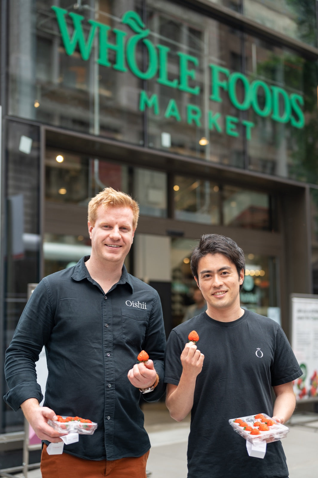 ホールフーズマーケットの店先でいちごを手に笑う創業者の2人
